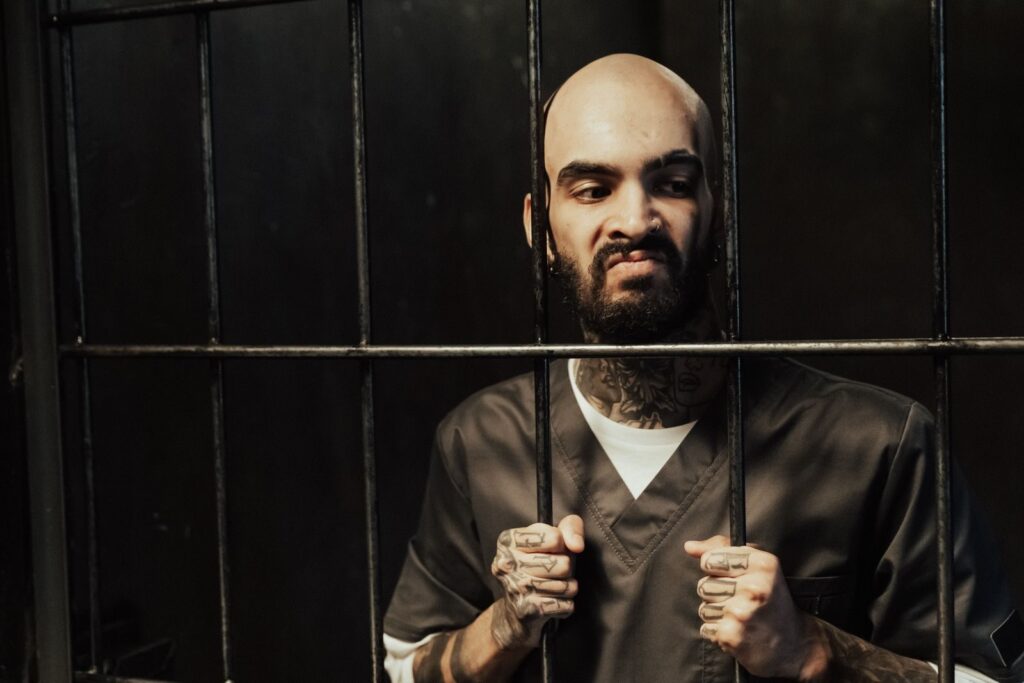 Bald bearded man with tattoos imprisoned behind bars, expressing strong emotions.
